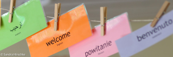 Willkommensschilder in verschiedenen Sprachen hängen an einer Leine